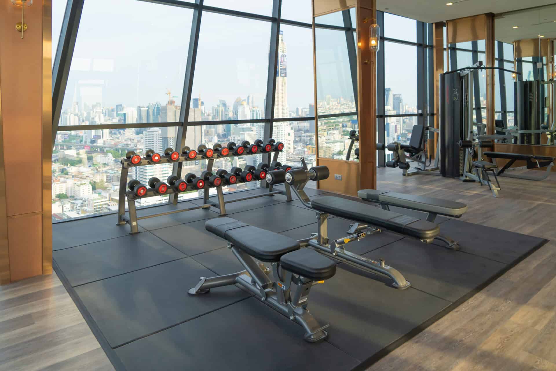 Dumbbells weights in Modern fitness center club with gym equipment decoration in sport or recreation concept. Working out. Interior design background with Bangkok City view, Thailand